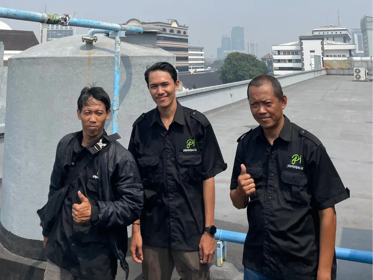 Tiga teknisi PipaPipa.id berseragam di rooftop gedung, berdiri di samping toren air yang baru dicuci